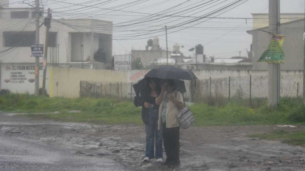 Three people sharing an umbrella in heavy rain on a muddy street.