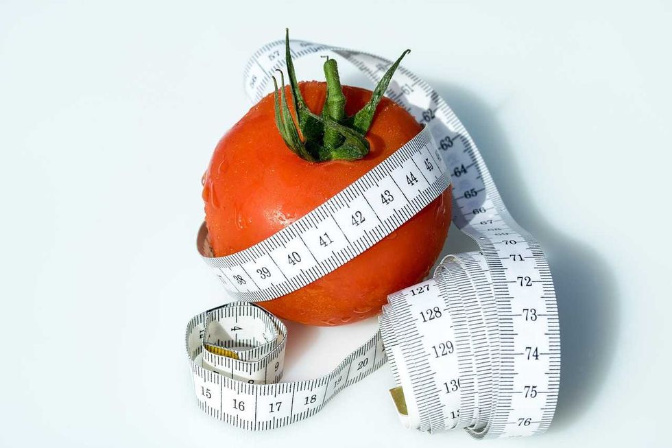 Tomato wrapped in a white measuring tape on a white background.