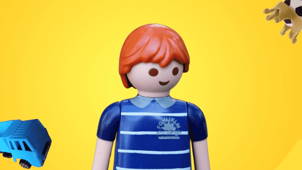 Toy figure with red hair and striped shirt, blue toy truck, giraffe parts on yellow background.