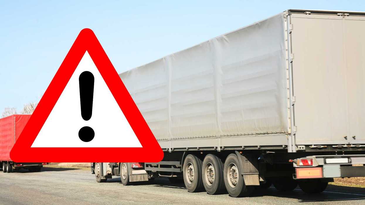 Truck on road with large warning sign in foreground.