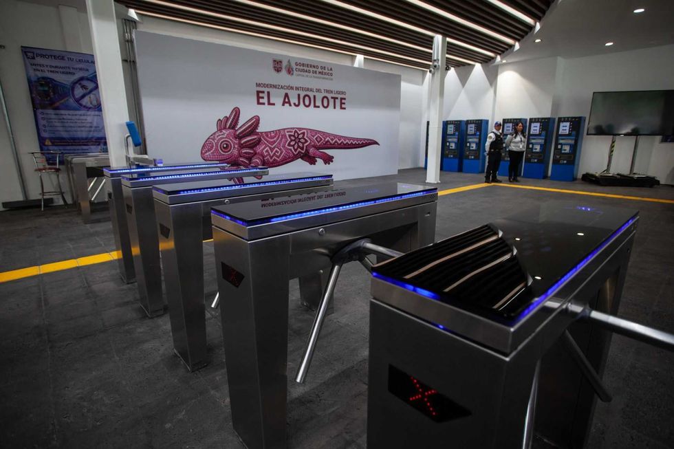 Turnstiles at a modern train station, "El Ajolote," with a decorative mural behind.