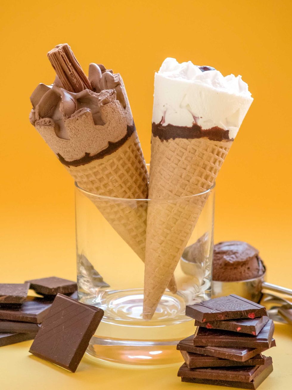 Two ice cream cones in a glass with chocolate pieces on an orange background.