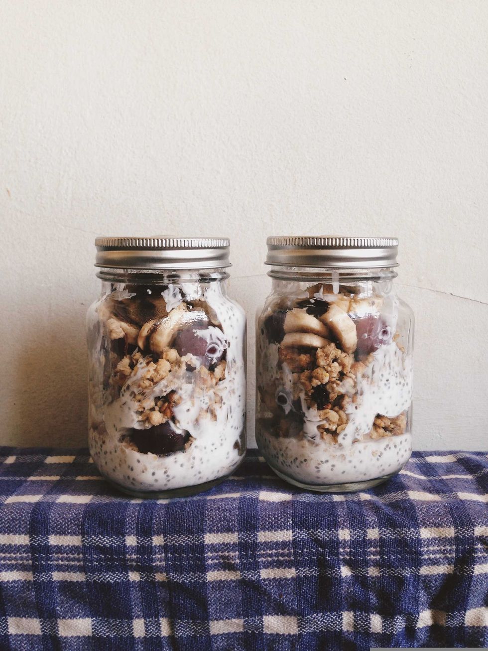 Two jars of chia pudding with granola and fruit on a checkered cloth.