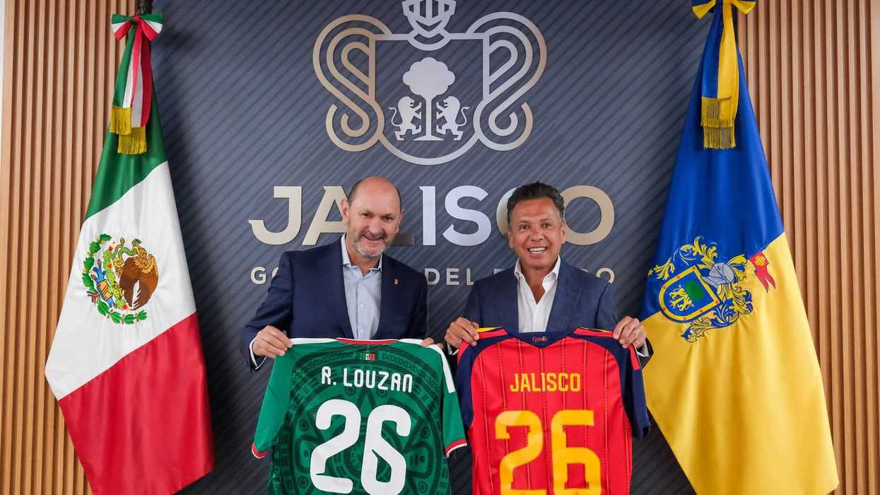 Two men hold soccer jerseys in front of flags and a Jalisco emblem.