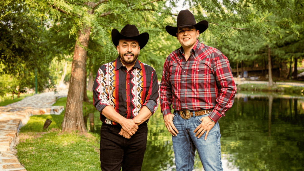 Two men in cowboy hats and patterned shirts standing by a pond in a lush park.