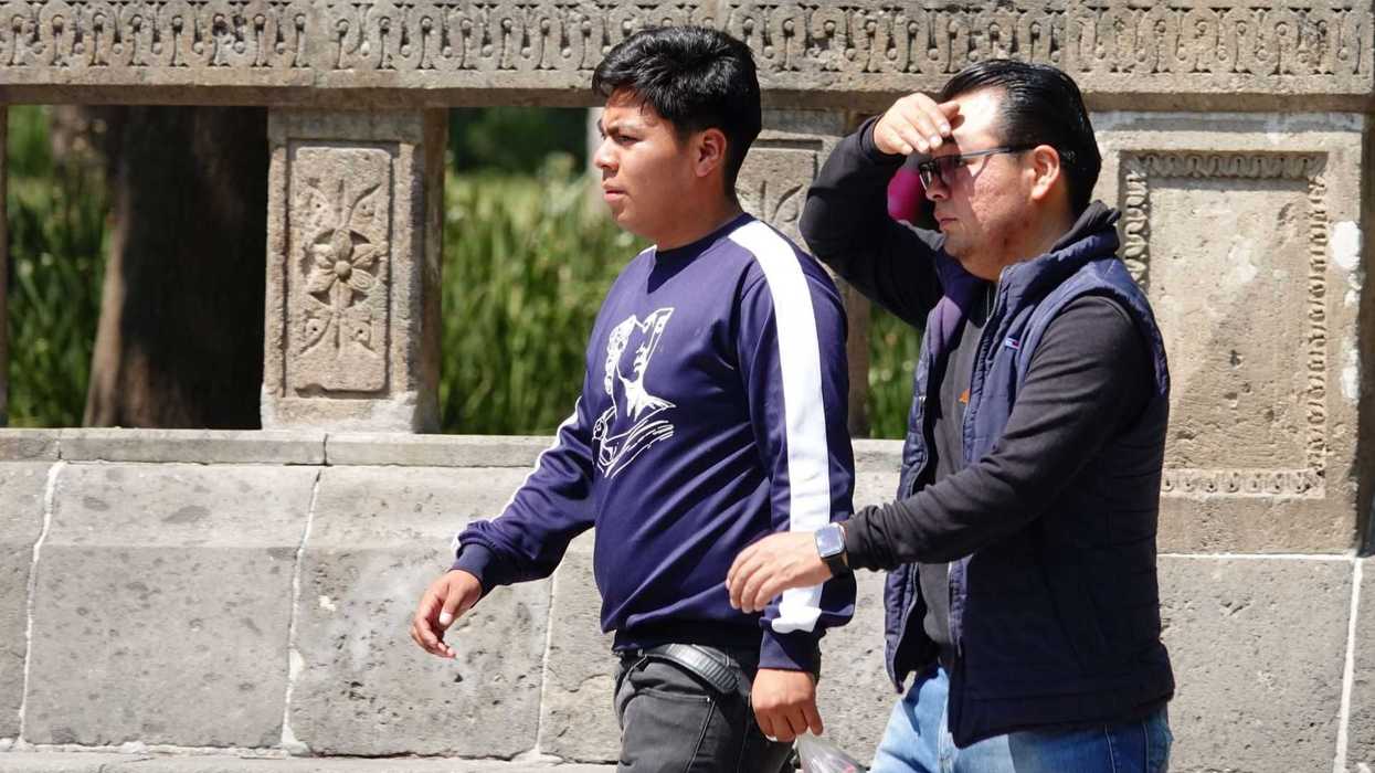 Two men walking outdoors; one shields eyes from sunlight.