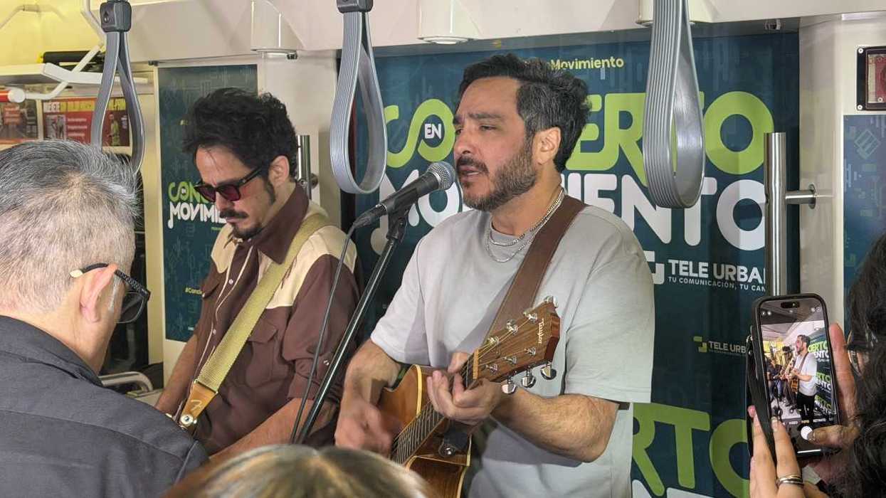 Two musicians perform with guitars inside a crowded transit vehicle as a passenger records them.