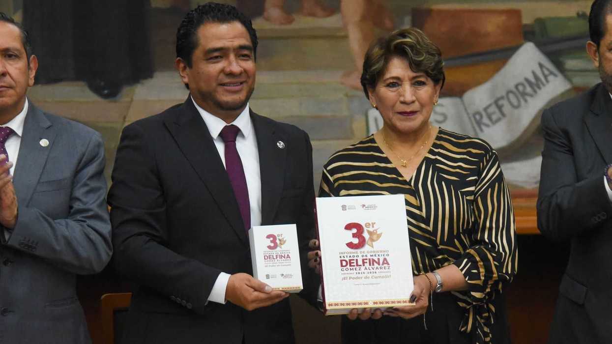 Two people holding books at a formal event, with others applauding beside them.