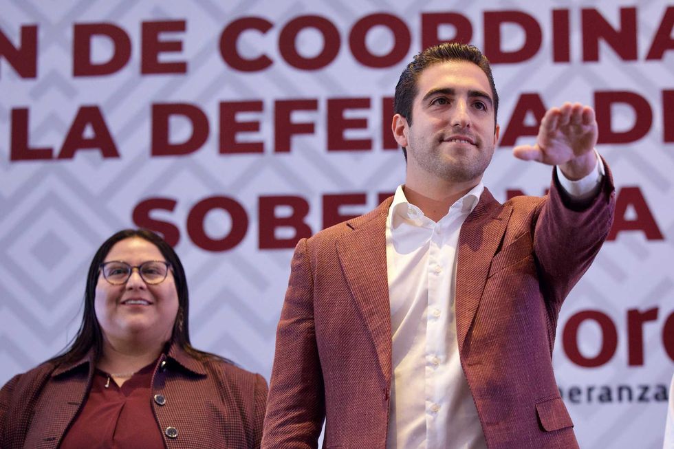 Two people in front of a large banner, one raising their hand.