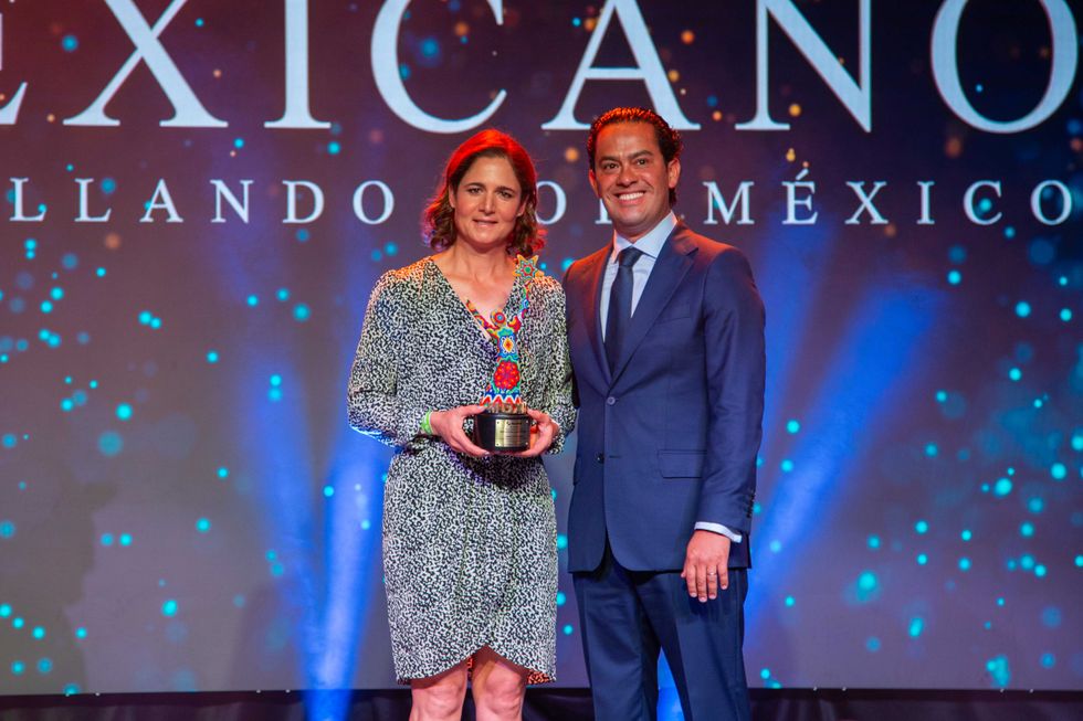 Two people posing with an award on stage, vibrant lights in the background.