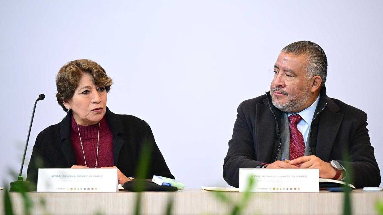 Two people seated at a table with microphones, engaged in conversation.