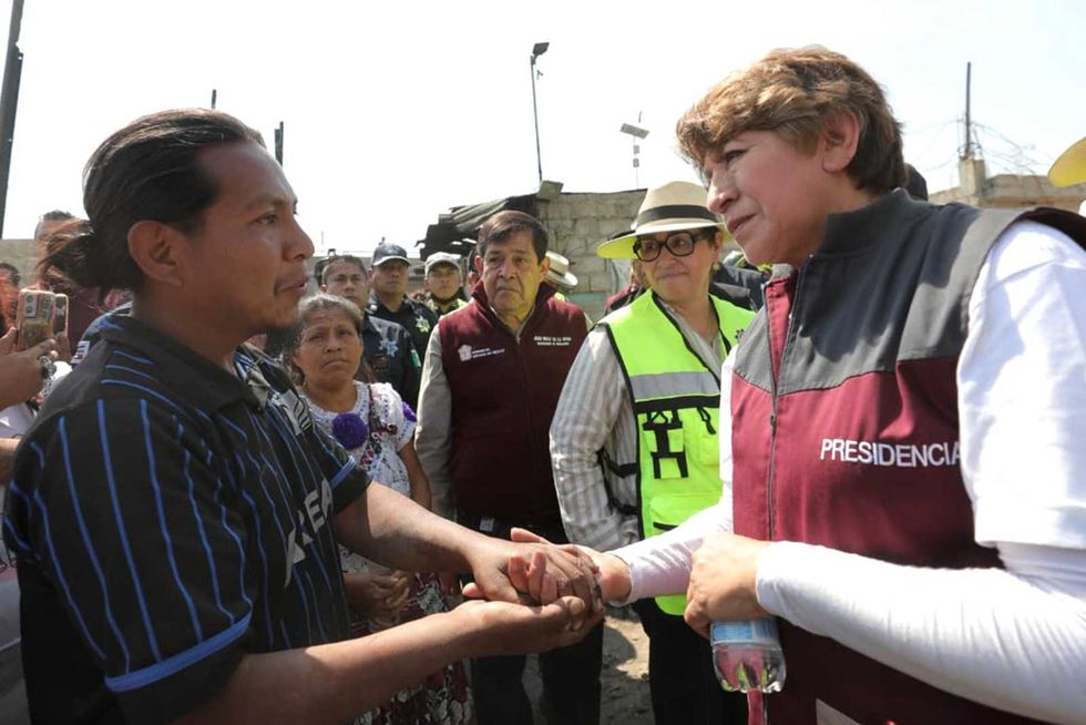 Two people shaking hands in a group, one wearing a "Presidencia" vest.