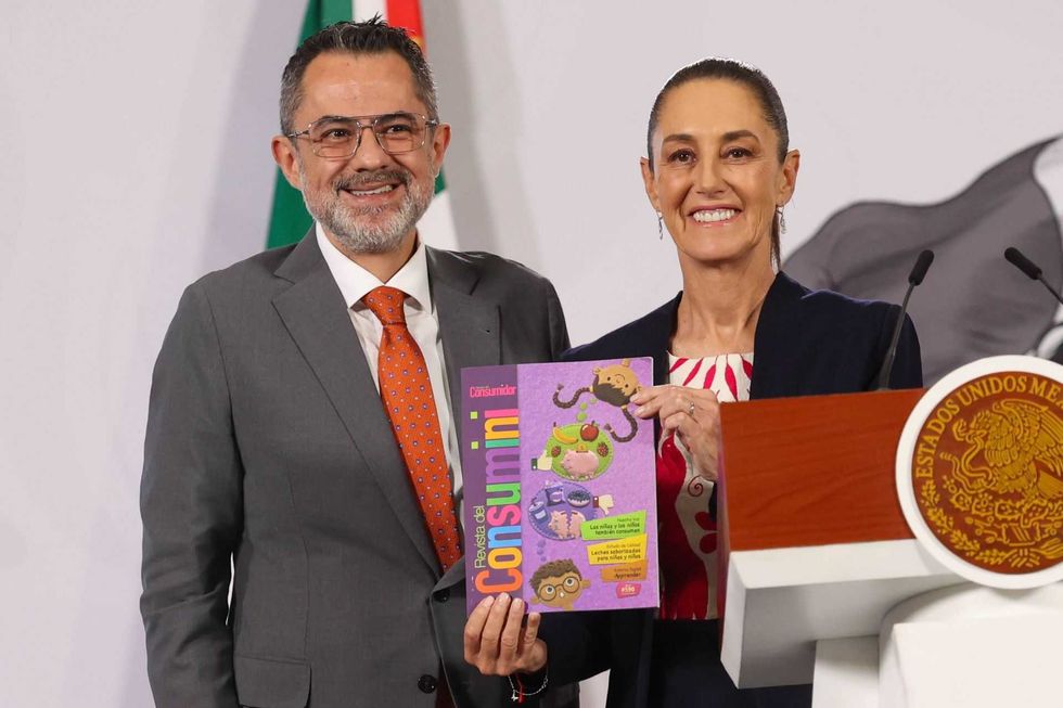 Two people smiling, holding a colorful magazine at a podium with a Mexican seal.