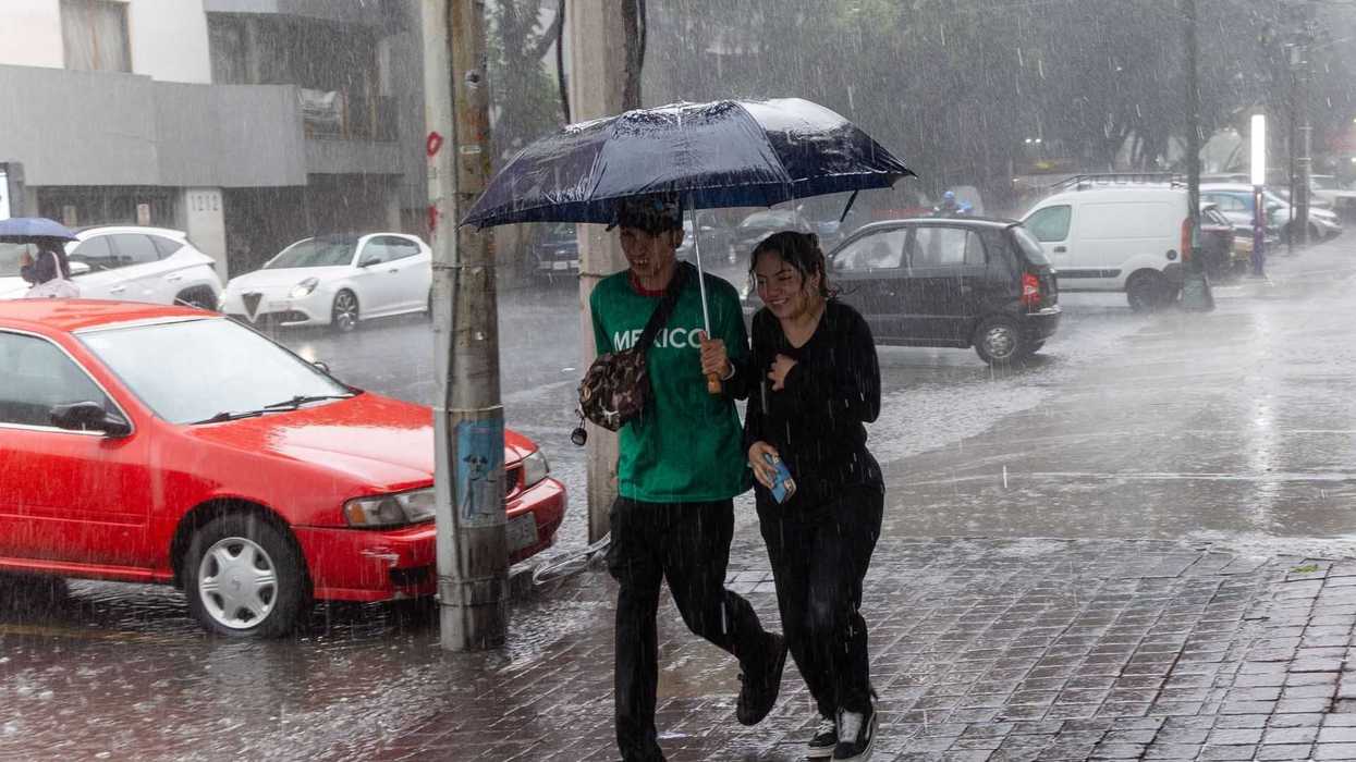 Two people under an umbrella walking in heavy rain on a city street.
