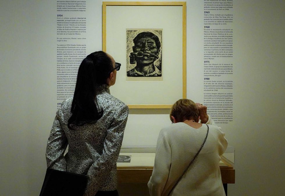 Two people view an artwork in a gallery, surrounded by descriptive text on the walls.