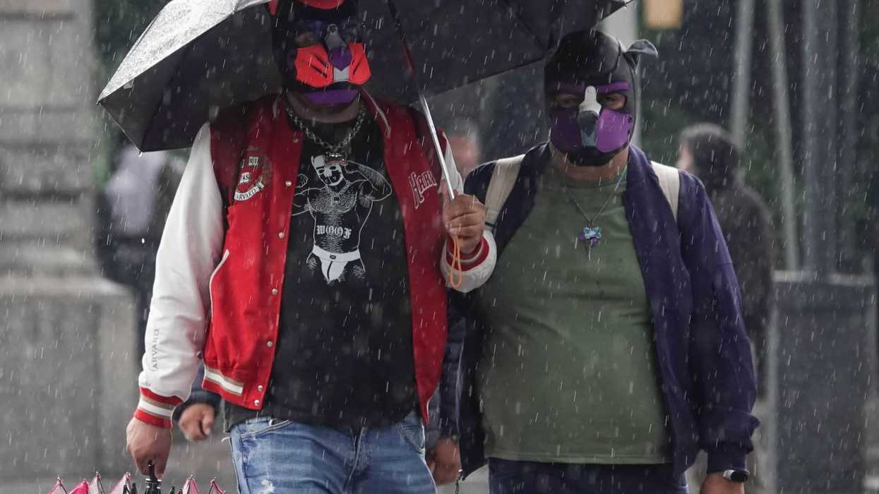 Two people wearing masks and sharing an umbrella in the rain.