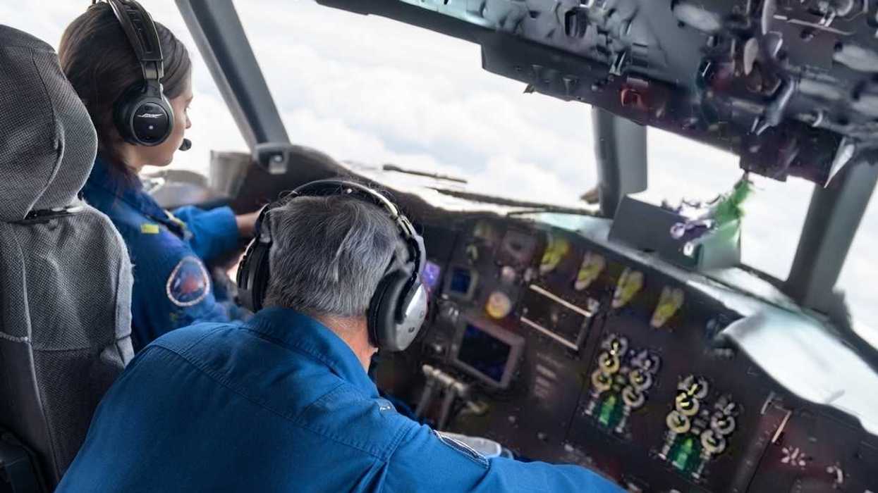 Two pilots in a cockpit flying through the clouds, wearing blue uniforms and headsets.