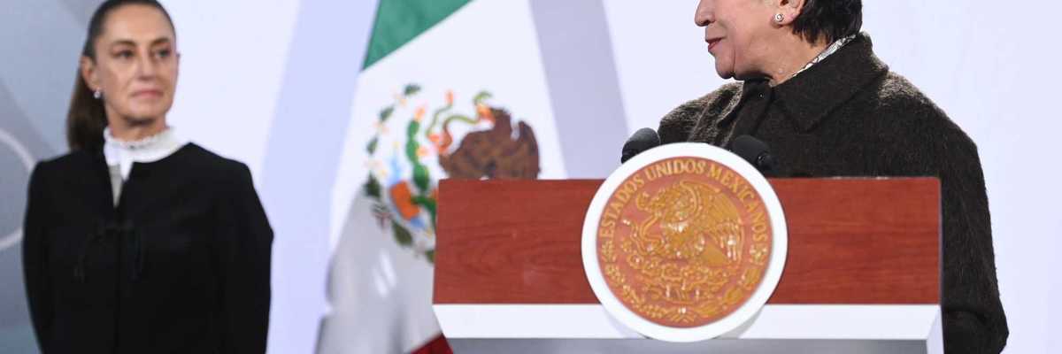 Two women at a podium, with a Mexican flag in the background.