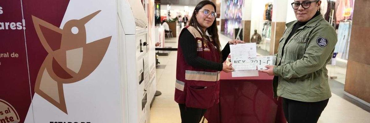 Two women exchange documents in front of a booth in a shopping mall.