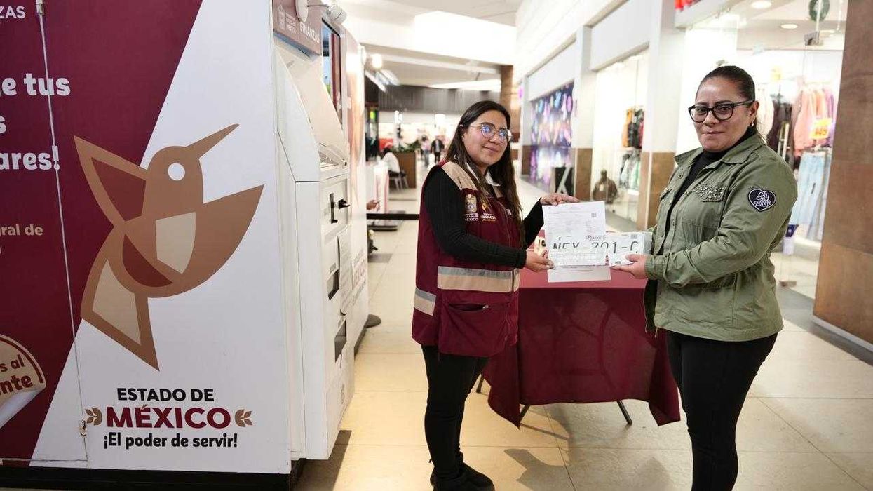 Two women exchange documents in front of a booth in a shopping mall.