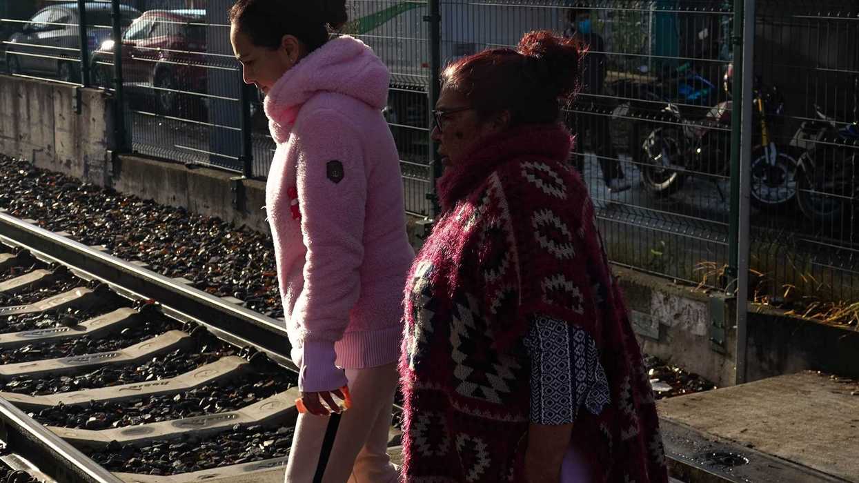Two women in winter attire walking near train tracks.