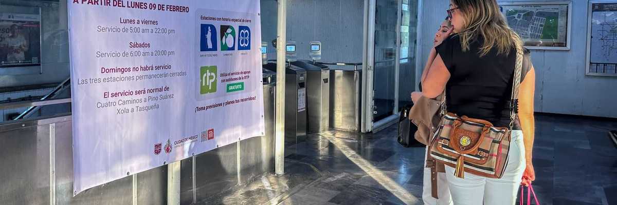 Two women reading a sign with metro service changes in a station entrance.
