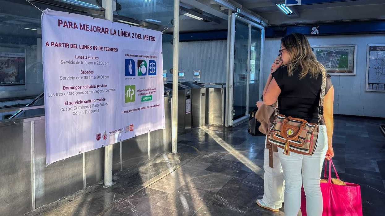Two women reading a sign with metro service changes in a station entrance.
