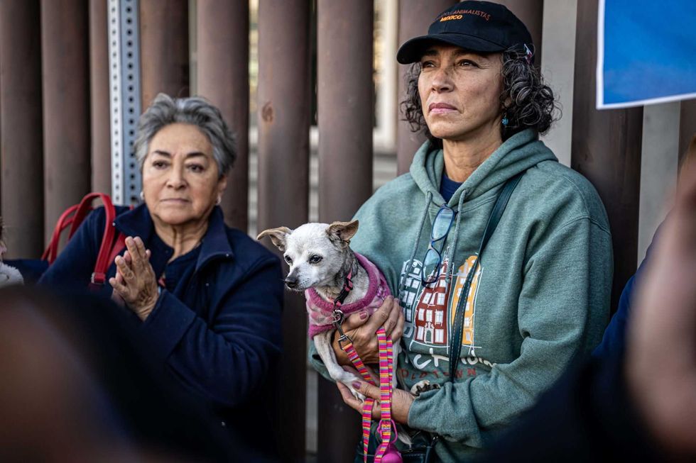 Two women seated outdoors, one holding a small dog in a pink outfit.