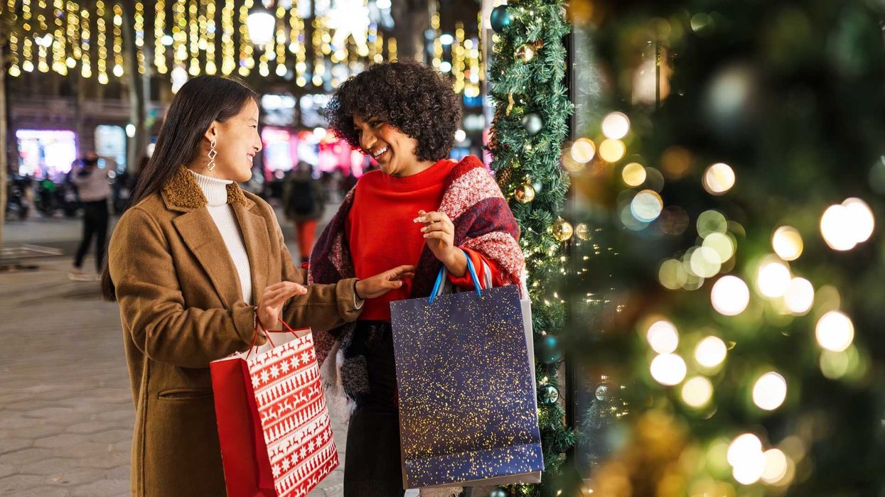 Two women smiling with shopping bags near festive holiday lights and decorations.