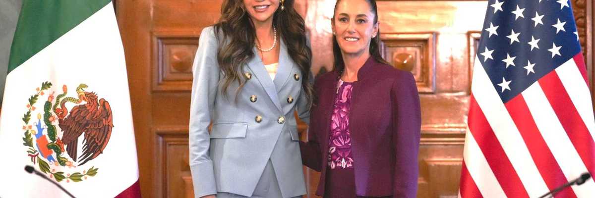Two women standing between Mexican and U.S. flags in a formal meeting room.