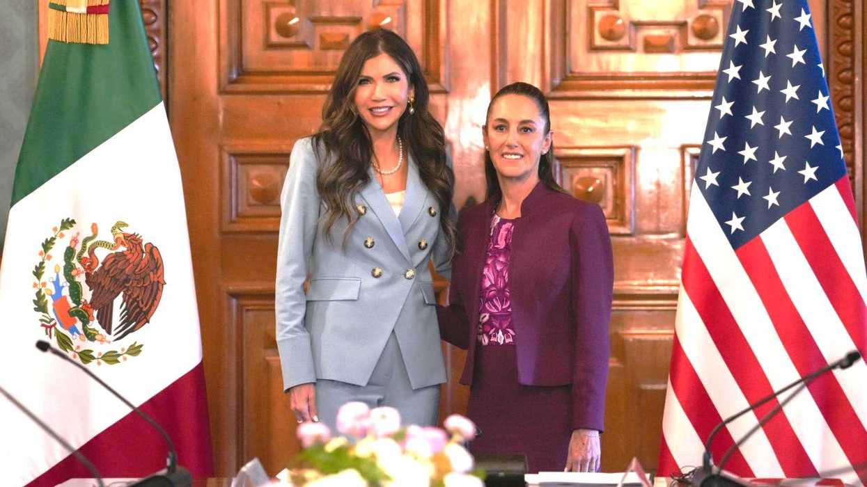 Two women standing between Mexican and U.S. flags in a formal meeting room.