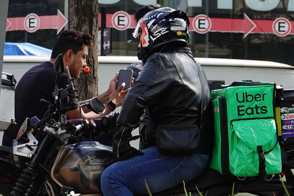 Uber Eats rider on a motorcycle interacting with a man on the street.
