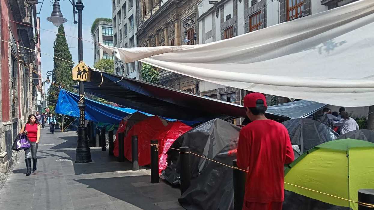 Urban street with tents, pedestrians, and overhead tarps creating shade.