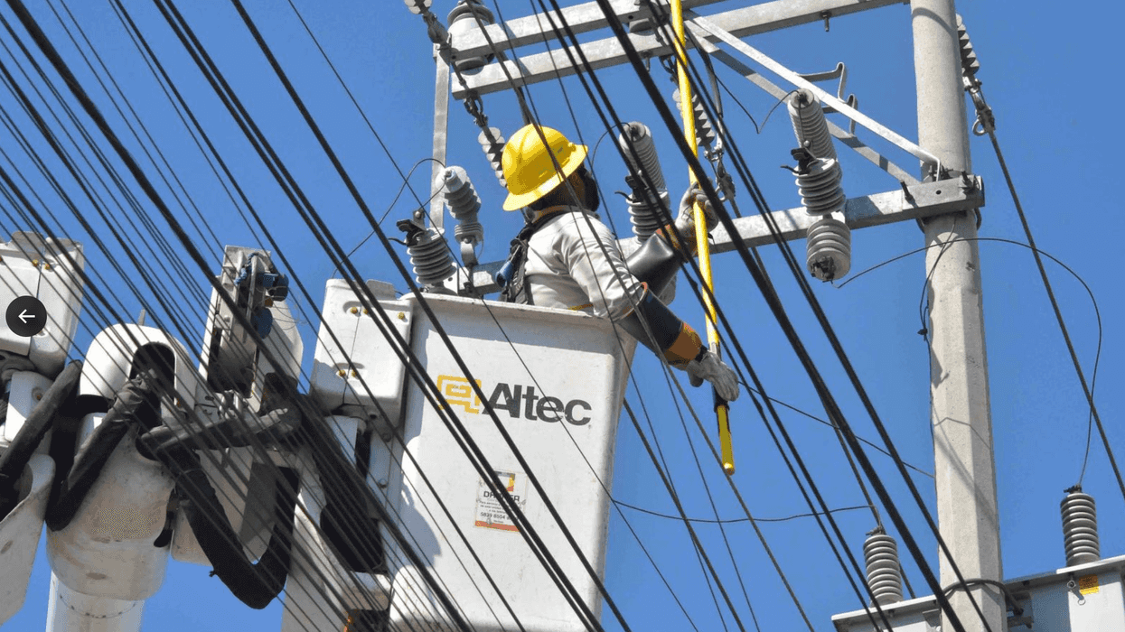 Utility worker in a lift repairs power lines on a sunny day.