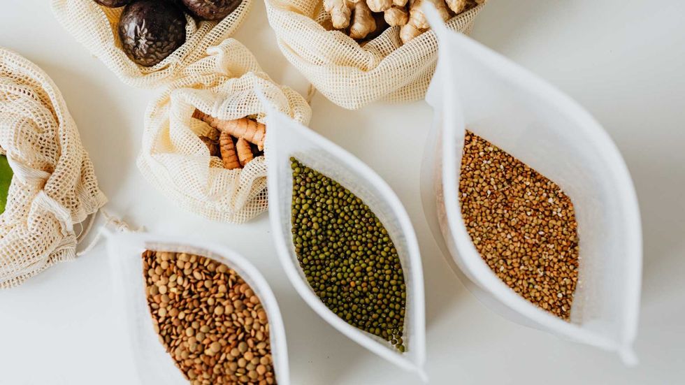 Various nuts and seeds in eco-friendly mesh bags on a white surface.