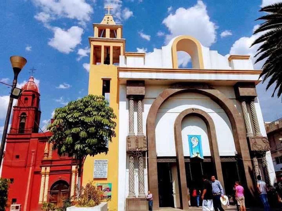 Vibrant church fa\u00e7ade with red and yellow towers under a blue sky with fluffy clouds.