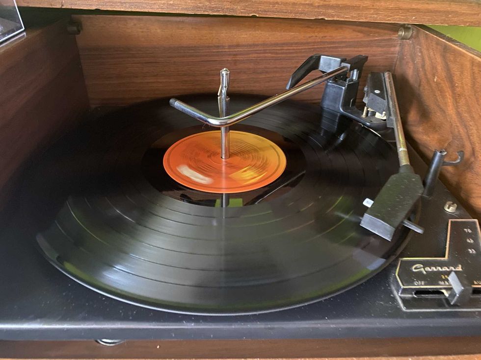 Vinyl record playing on vintage turntable with wooden cabinet detail.