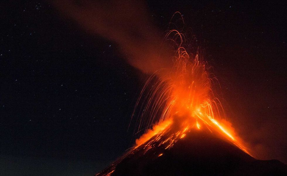 Volcano erupting at night, spewing bright orange lava and dark smoke under a starry sky.