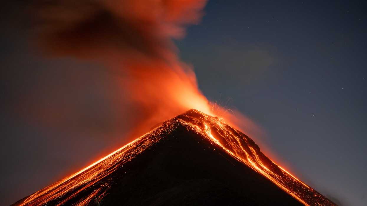 Volcano erupting at night, spewing lava and ash into the sky.