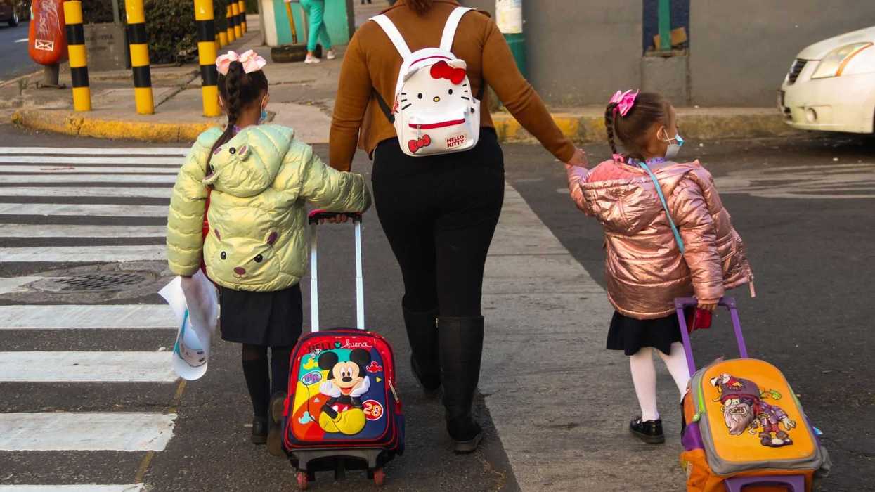 Woman and two children with backpacks and rolling suitcases crossing the street.