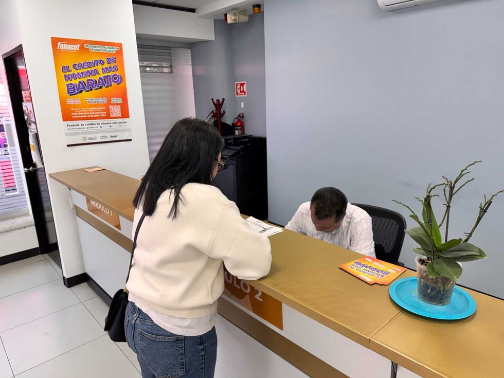 Woman at a bank counter interacting with an employee, plant on desk.