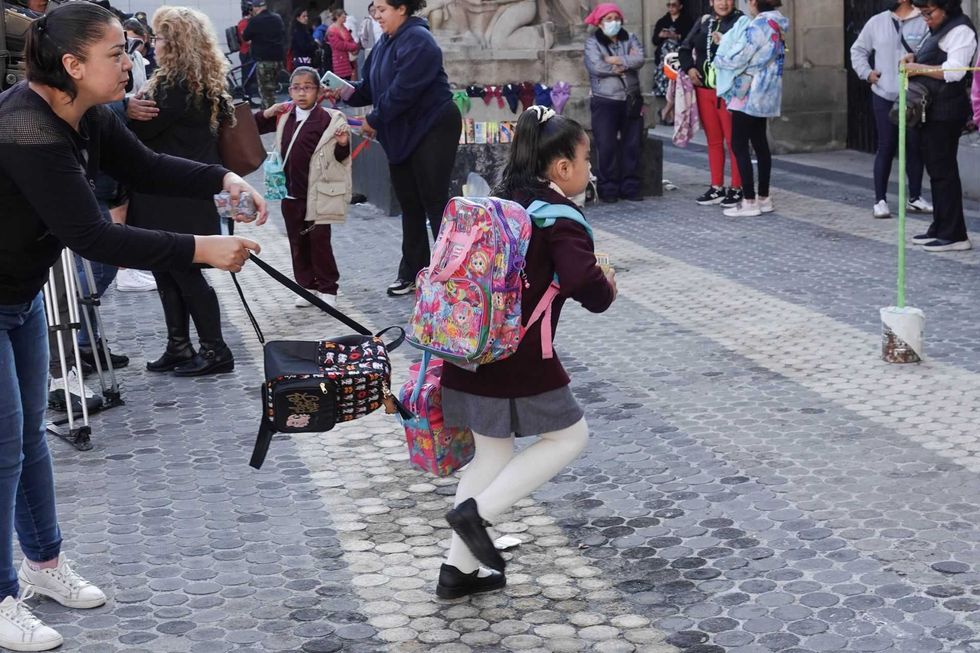 Woman handing bags to a girl with a colorful backpack in a busy street.