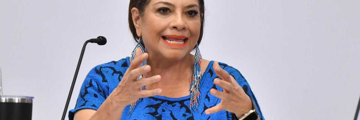 Woman in blue speaks passionately at a microphone, gesturing with her hands.