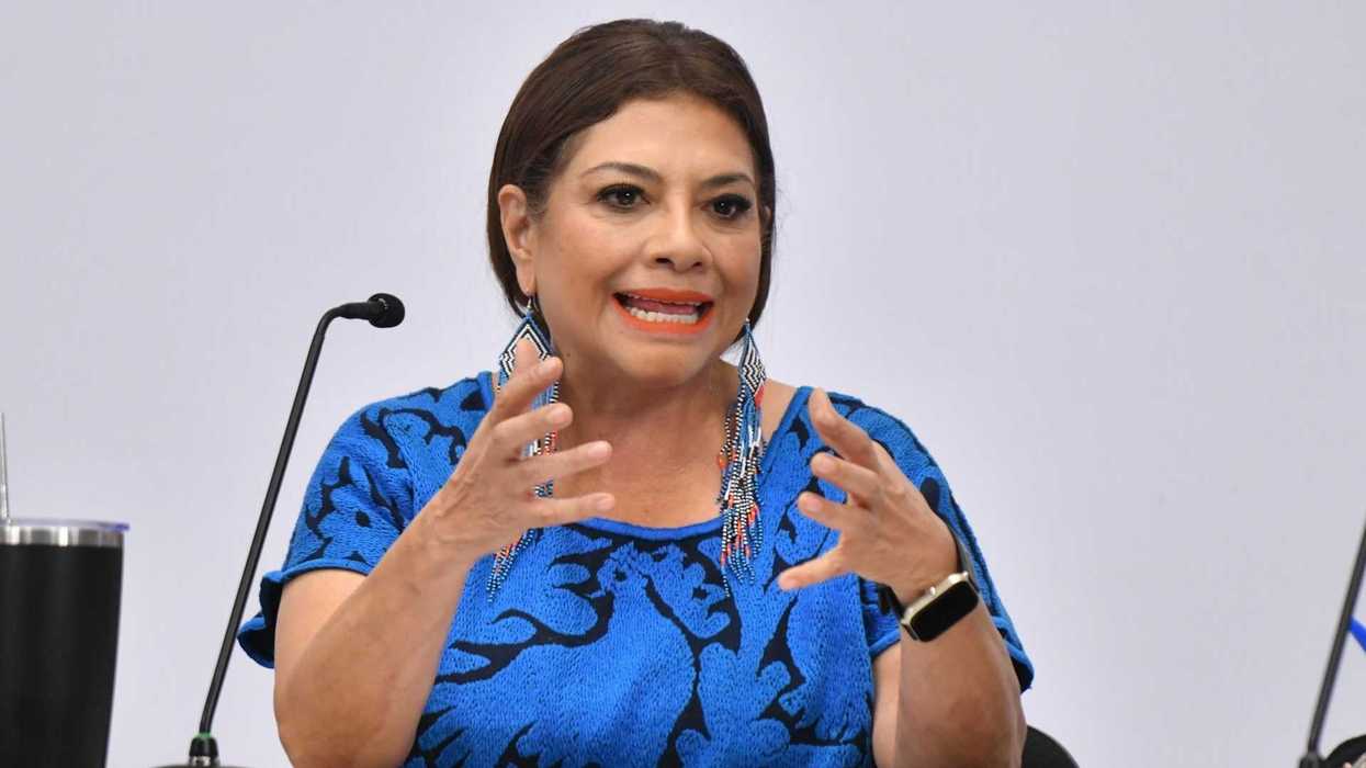 Woman in blue speaks passionately at a microphone, gesturing with her hands.