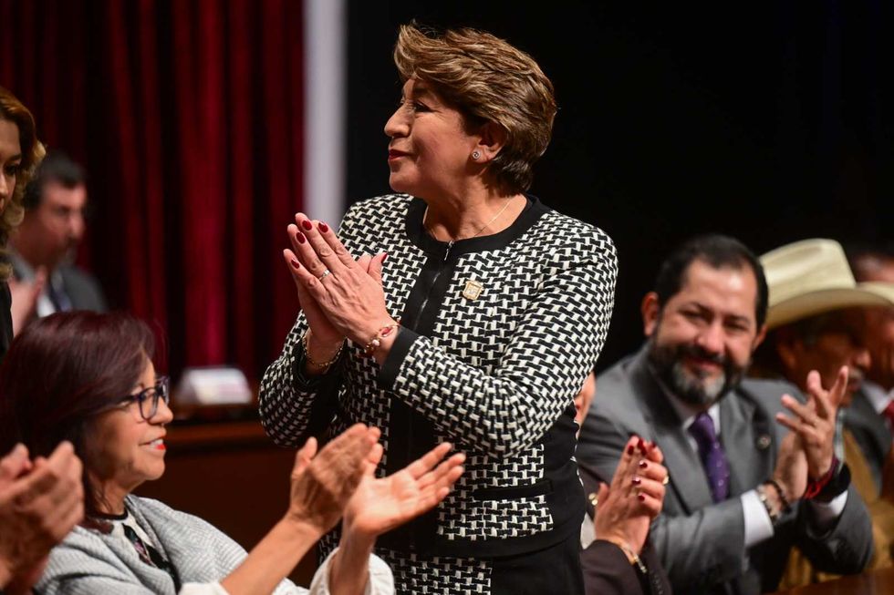 Woman in checkered suit applauding at an event, surrounded by others clapping.