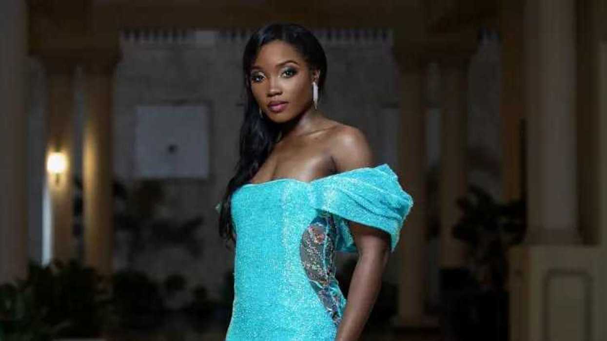 Woman in elegant turquoise gown poses in a dimly lit setting.