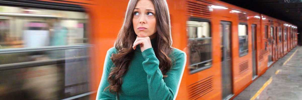 Woman in green sweater ponders as an orange train speeds past on a subway platform.