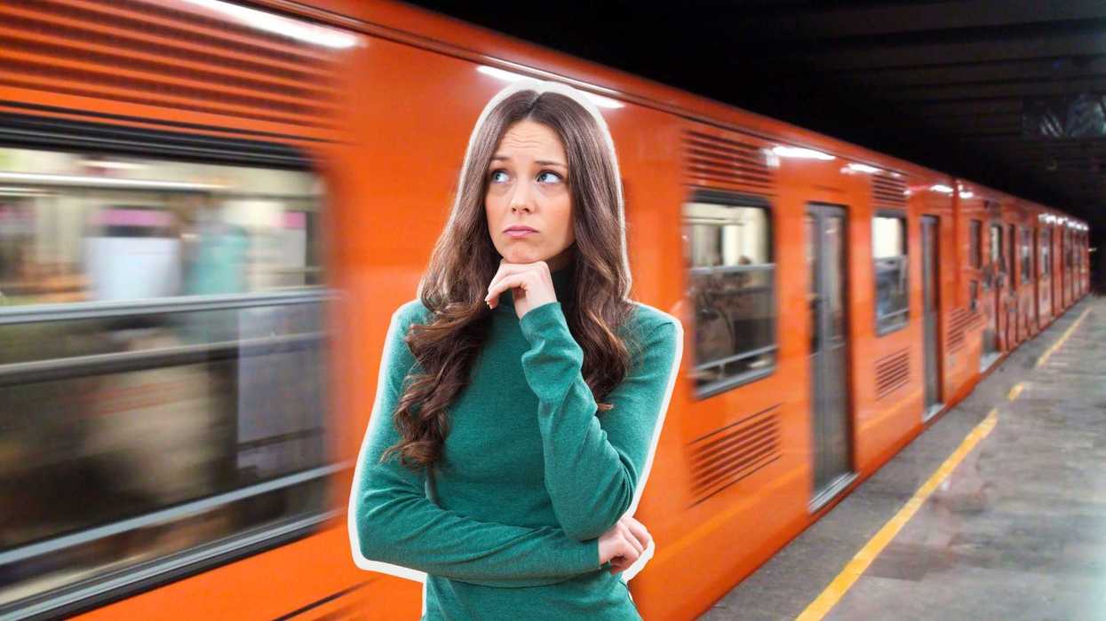 Woman in green sweater ponders as an orange train speeds past on a subway platform.