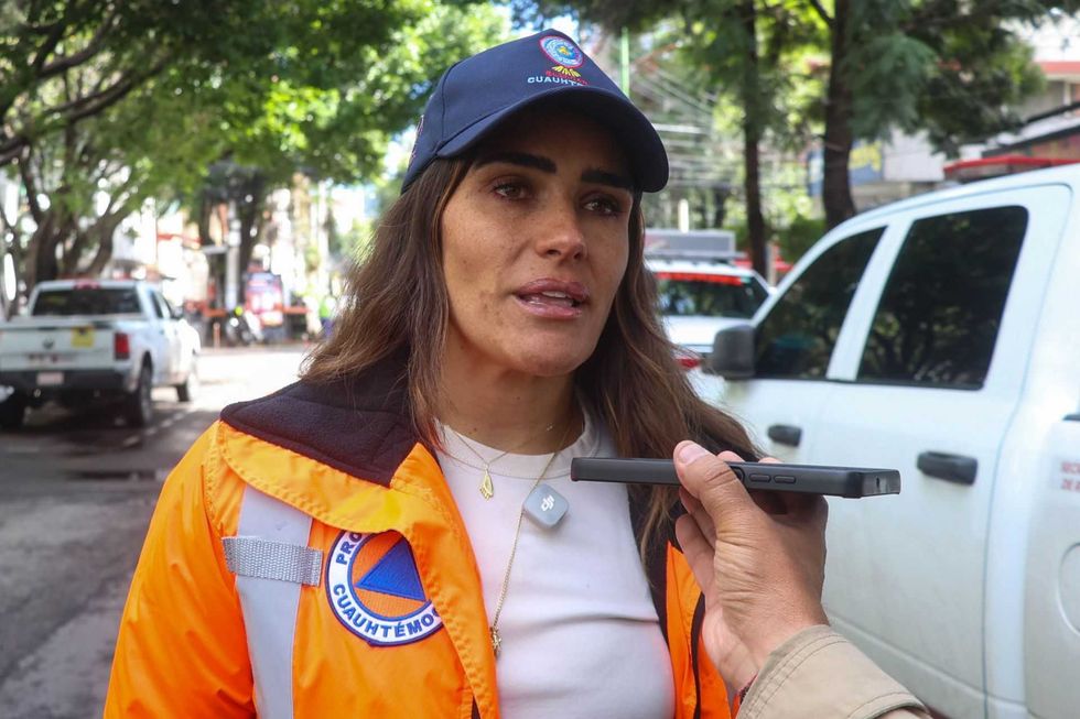 Woman in orange jacket and cap being interviewed outdoors.