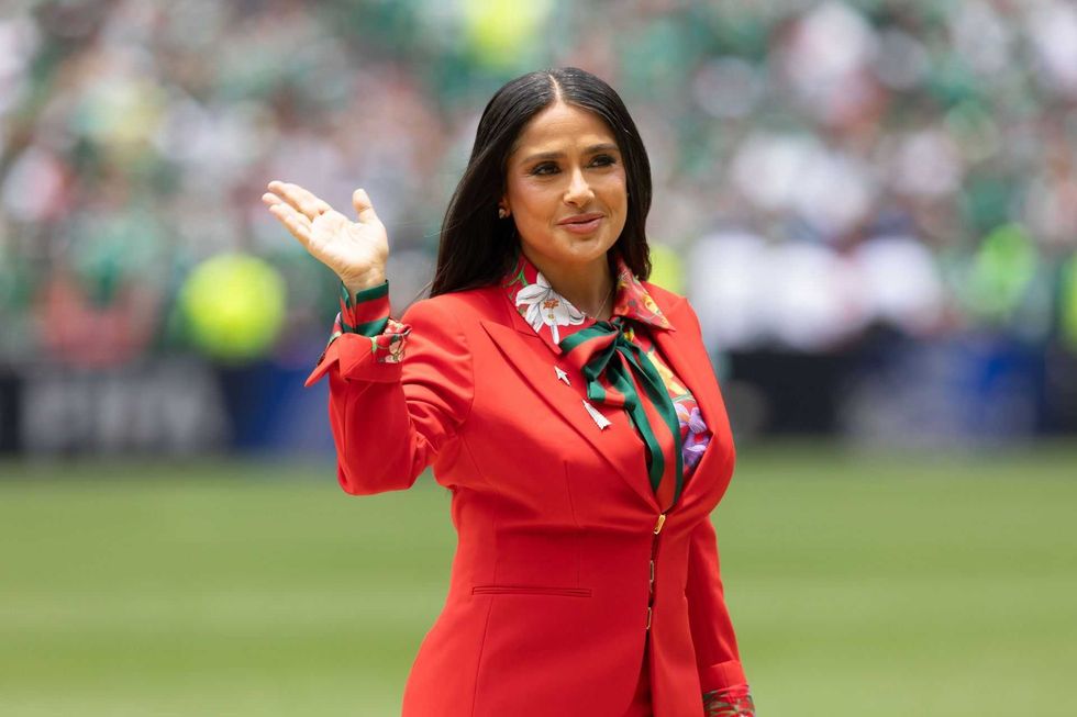 Woman in red suit waving on a sports field.